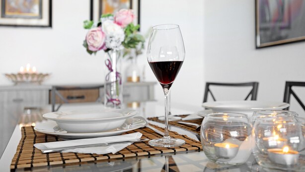 Una mesa de comedor dispuesta con platos, una copa de vino, velas y un florero con flores.