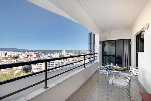 A balcony with a city view, a table with chairs, and a window with curtains.