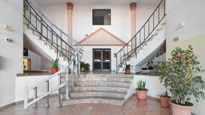 Un hall espacioso con una escalera central, plantas en macetas y un gran ventanal.
