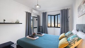 Un dormitorio con cama, mesita de noche, ventana con cortinas y vistas a la ciudad.