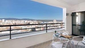 Un balcón con vistas a la ciudad, una mesa con sillas y un ventanal de vidrio.