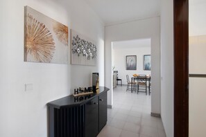A hallway with a black console table, a white wall with two artworks, and a dining area in the background.