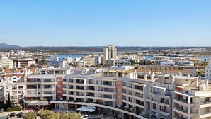 Un edificio residencial de varios pisos con balcones, un estacionamiento y vistas a una ciudad costera.