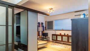 Een moderne kamer met een schuifdeurkast, een bank, een televisie en een raam met zonwering.