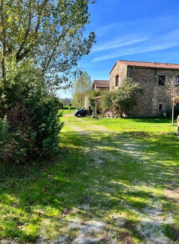 Un bâtiment en pierre, surmonté d’un toit recouvert de tuiles rouges, entouré d’une pelouse et d’arbres.