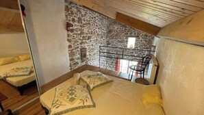 Een gezellige kamer met een houten plafond, een stenen muur en een bed met geel beddengoed.
