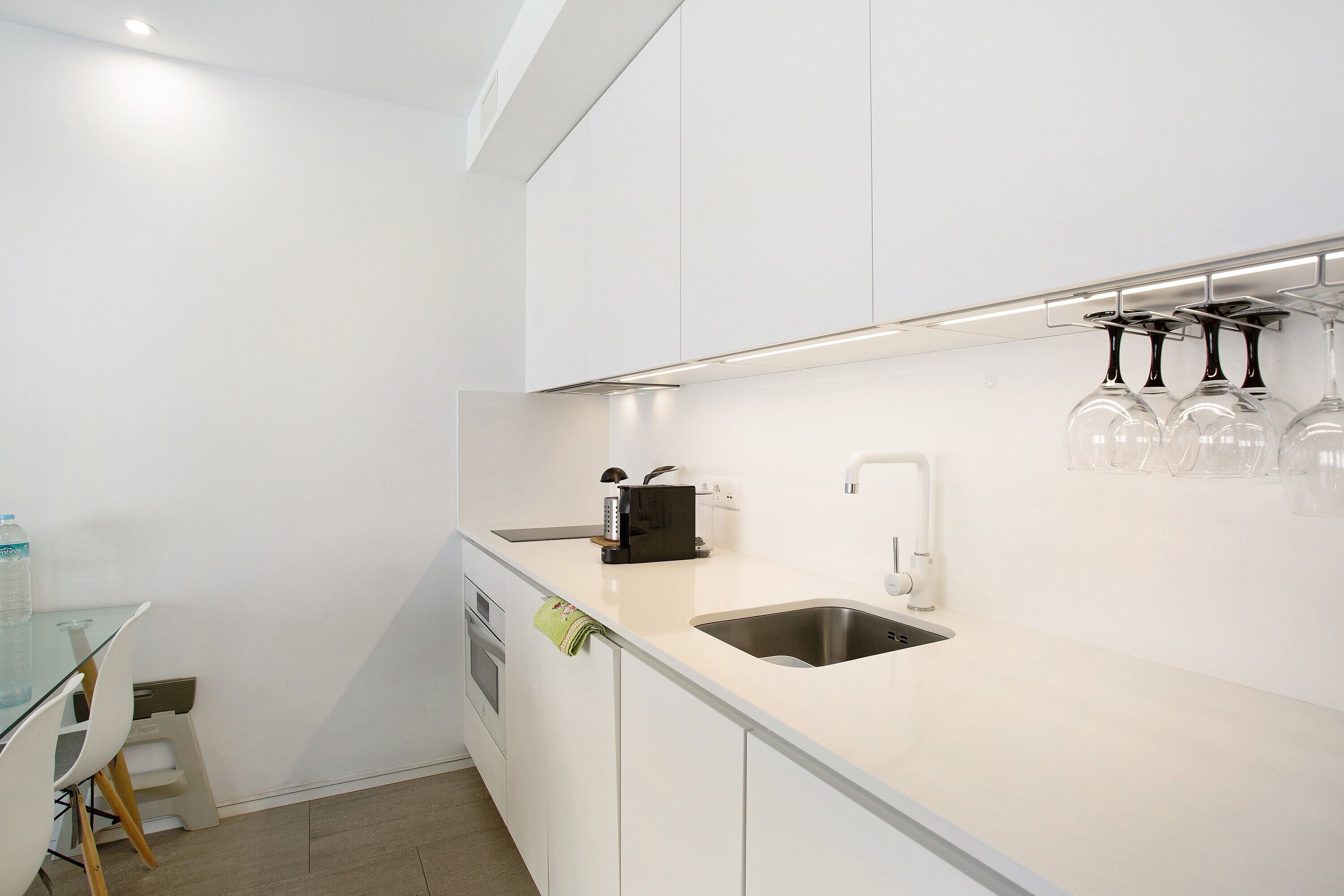 Una cocina moderna con un lavamanos de acero inoxidable, una mesa de vidrio y una estantería para vinos.