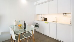 Une cuisine moderne avec des meubles blancs, une table à manger en verre et un four encastré.