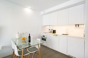 A modern kitchen with white cabinets, a glass dining table, and a built-in oven.