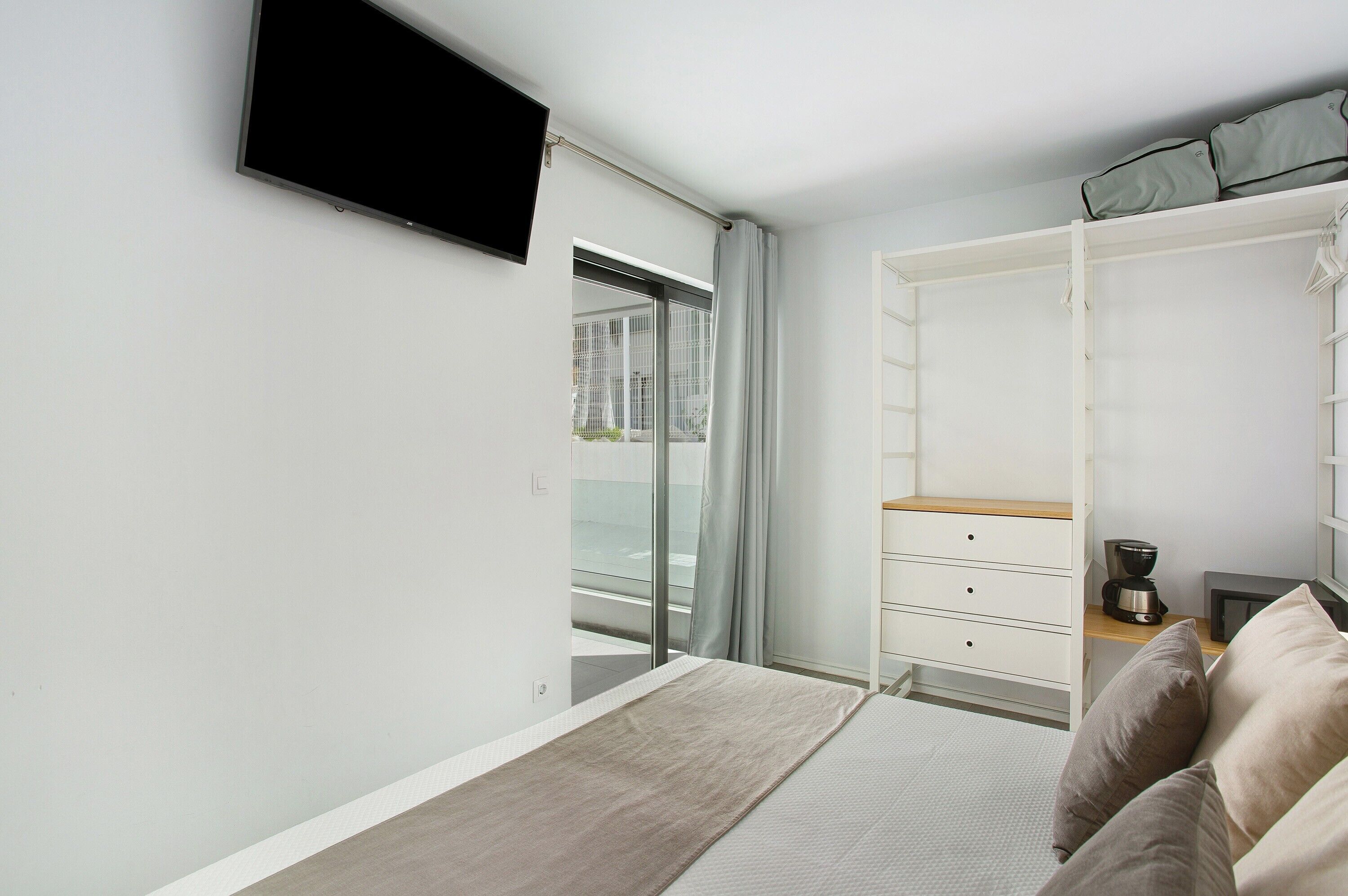 Un dormitorio con cama, televisor montado en la pared, armario y cafetera.