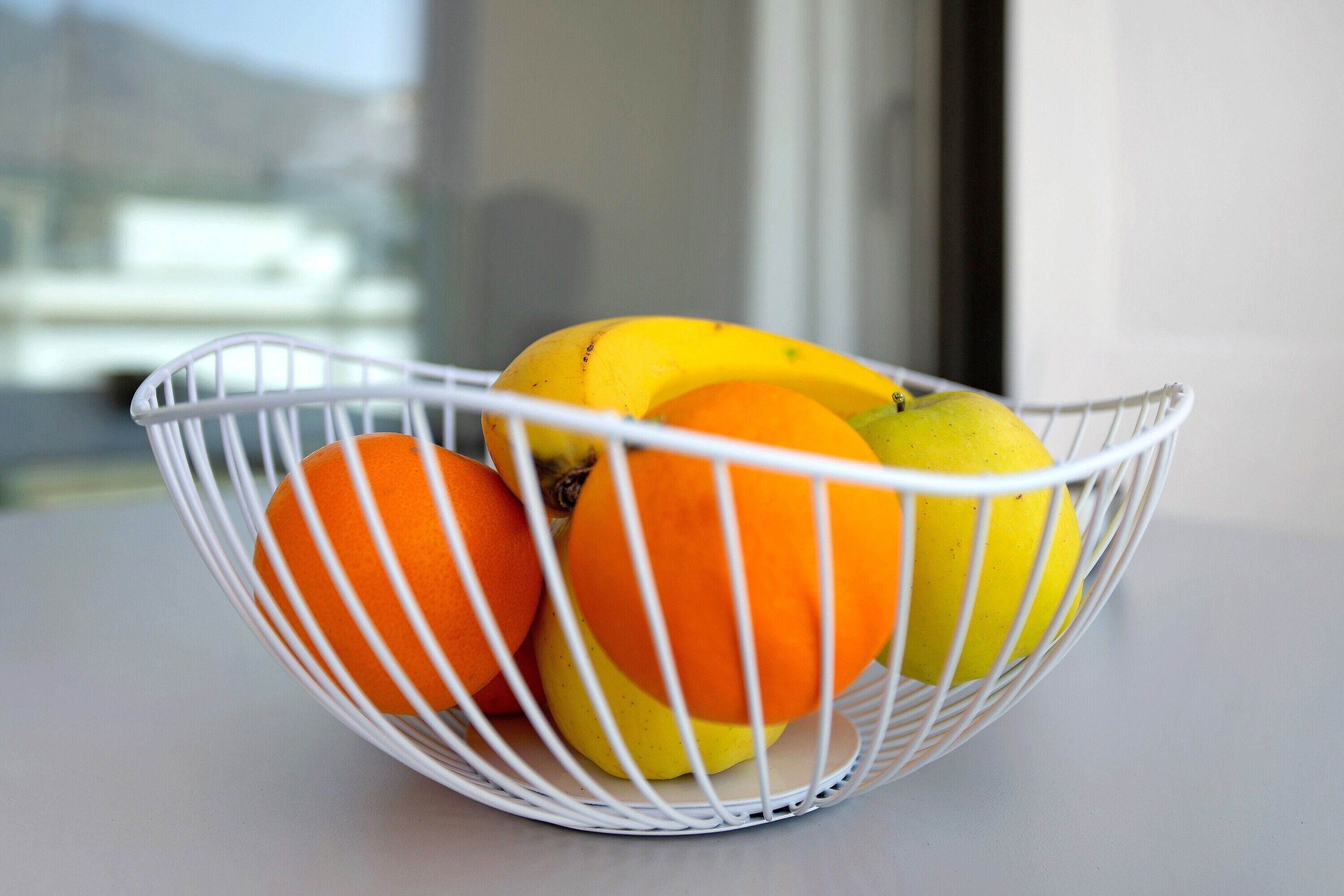 Una cesta de mimbre blanca con naranjas y un limón sobre una mesa.