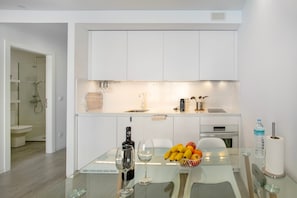 A modern kitchen with white cabinets, a glass table, a wine bottle, and a fruit bowl.