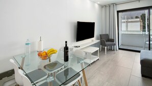 Ein modernes Wohnzimmer mit einem Glastisch, einem Flachbildfernseher, einer Couch und einem Balkon mit Aussicht.