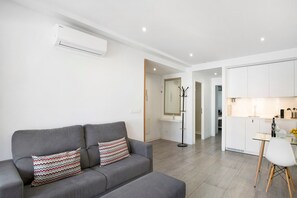 A modern living room with a grey sofa, a small table, and a kitchen area in the background.