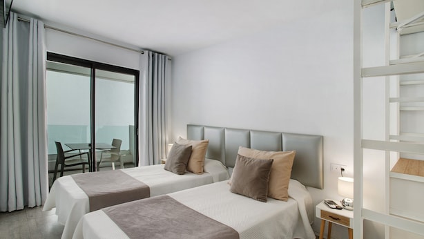 Ein Hotelzimmer mit zwei Betten, einem Schreibtisch, einem Sessel und Meerblick.