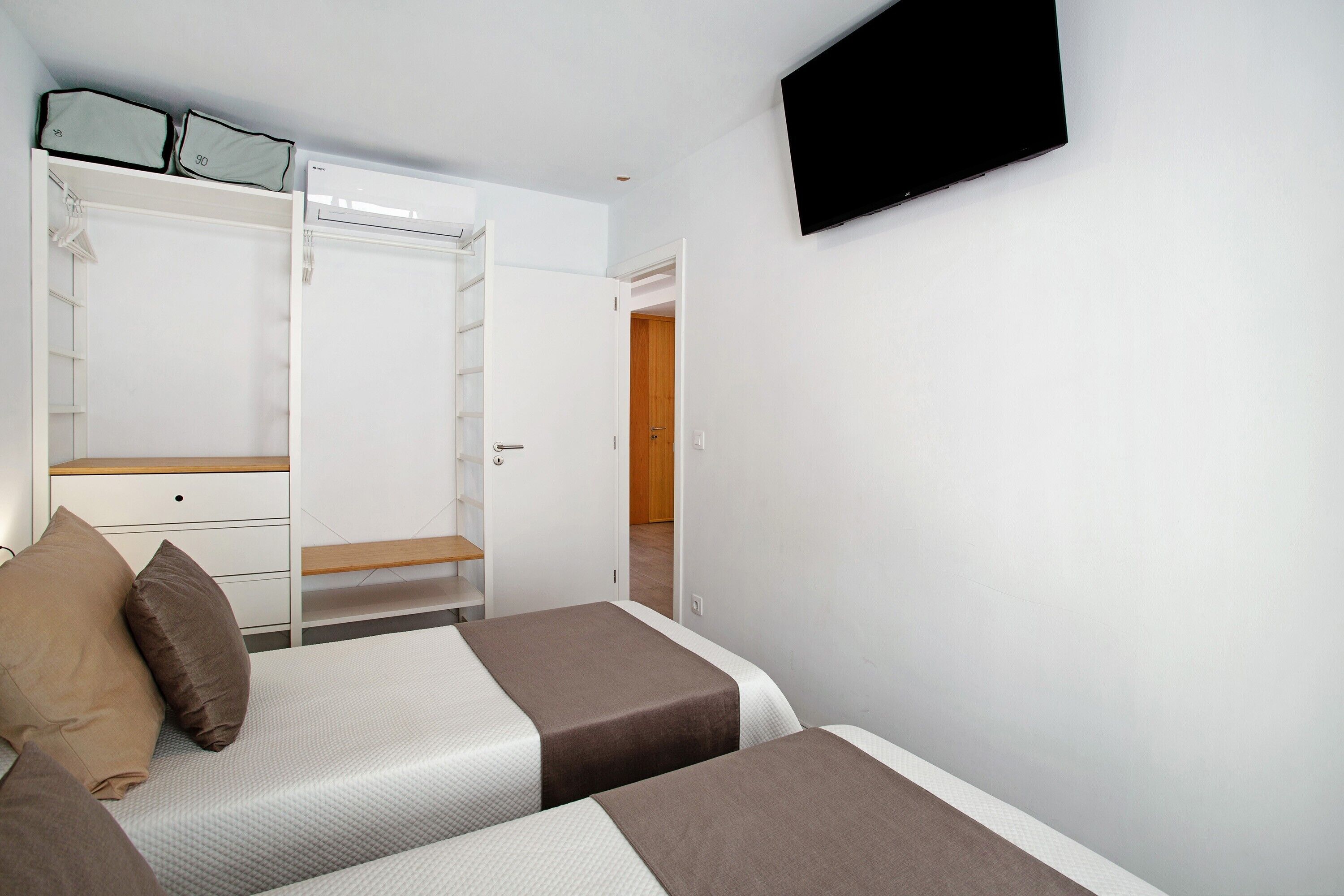 Un dormitorio con dos camas, un armario, un televisor y una puerta que da a otra habitación.
