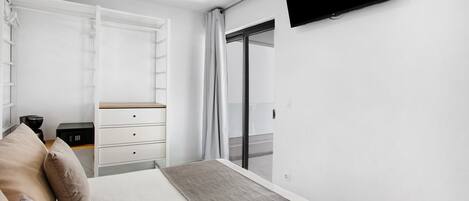 Un dormitorio moderno con cama, televisor, armario, escritorio y puerta corrediza a un balcón.