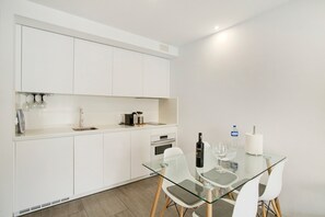 A modern kitchen with white cabinets, a glass dining table, and a built-in oven.