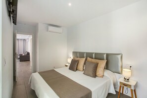 A hotel room with a bed, bedside tables, a lamp, and an air conditioning unit.