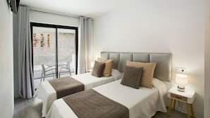 Habitación de hotel con dos camas, una mesita de noche, una lámpara y vistas al exterior.