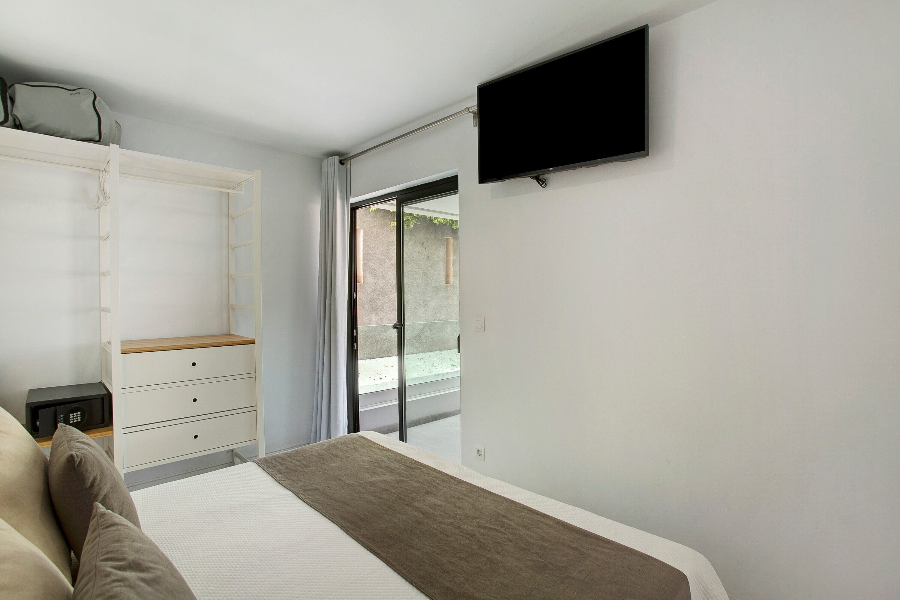 Een slaapkamer met een bed, een televisie, een kledingkast en een schuifdeur naar buiten.