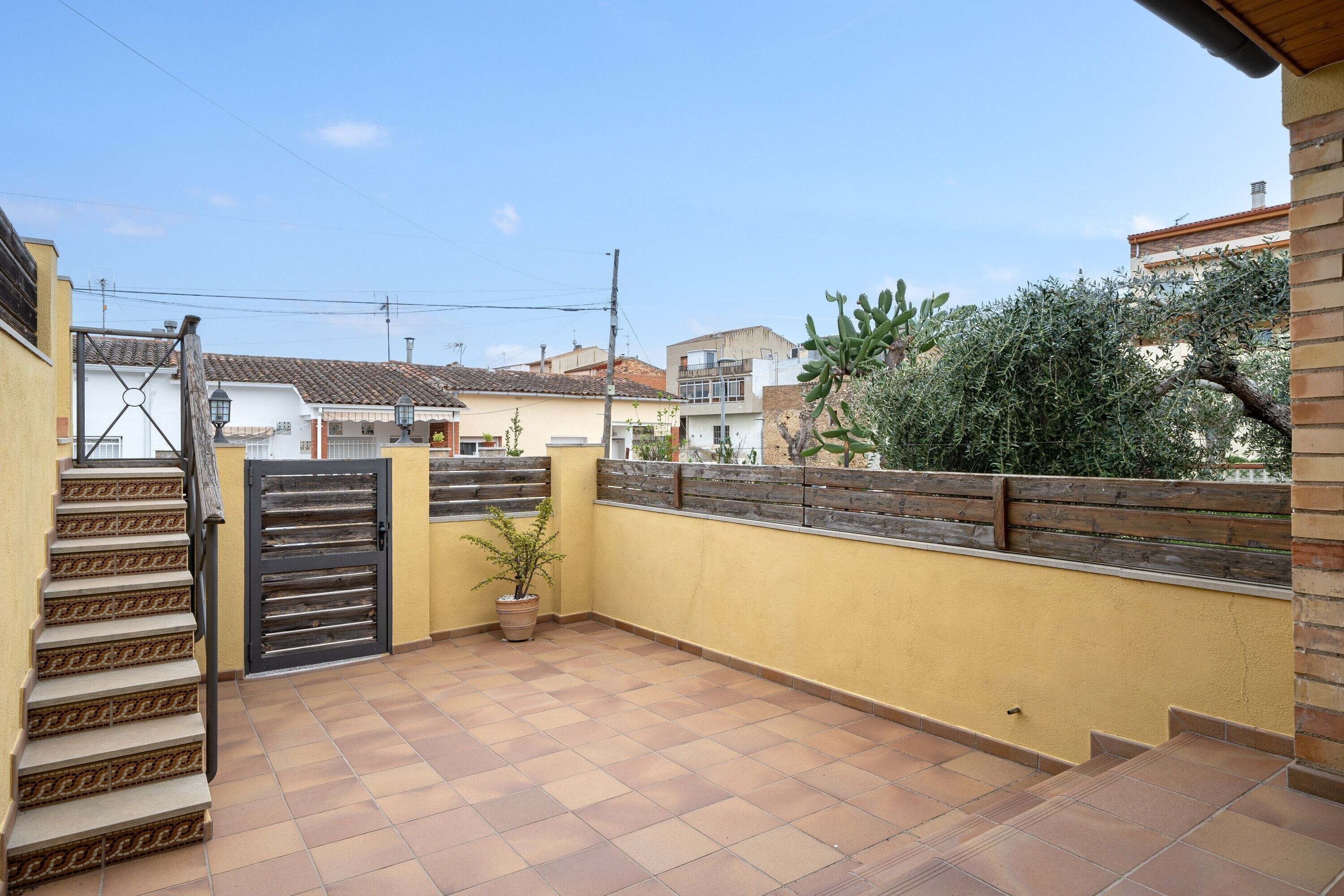 Een terras bij een woning, met betegelde vloer, houten schutting en een poort.