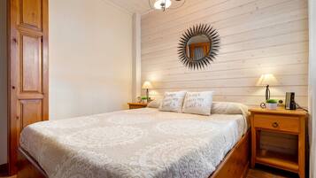 A bedroom with a large bed, wooden headboard, two bedside tables with lamps, a mirror, and a wall-mounted shelf.