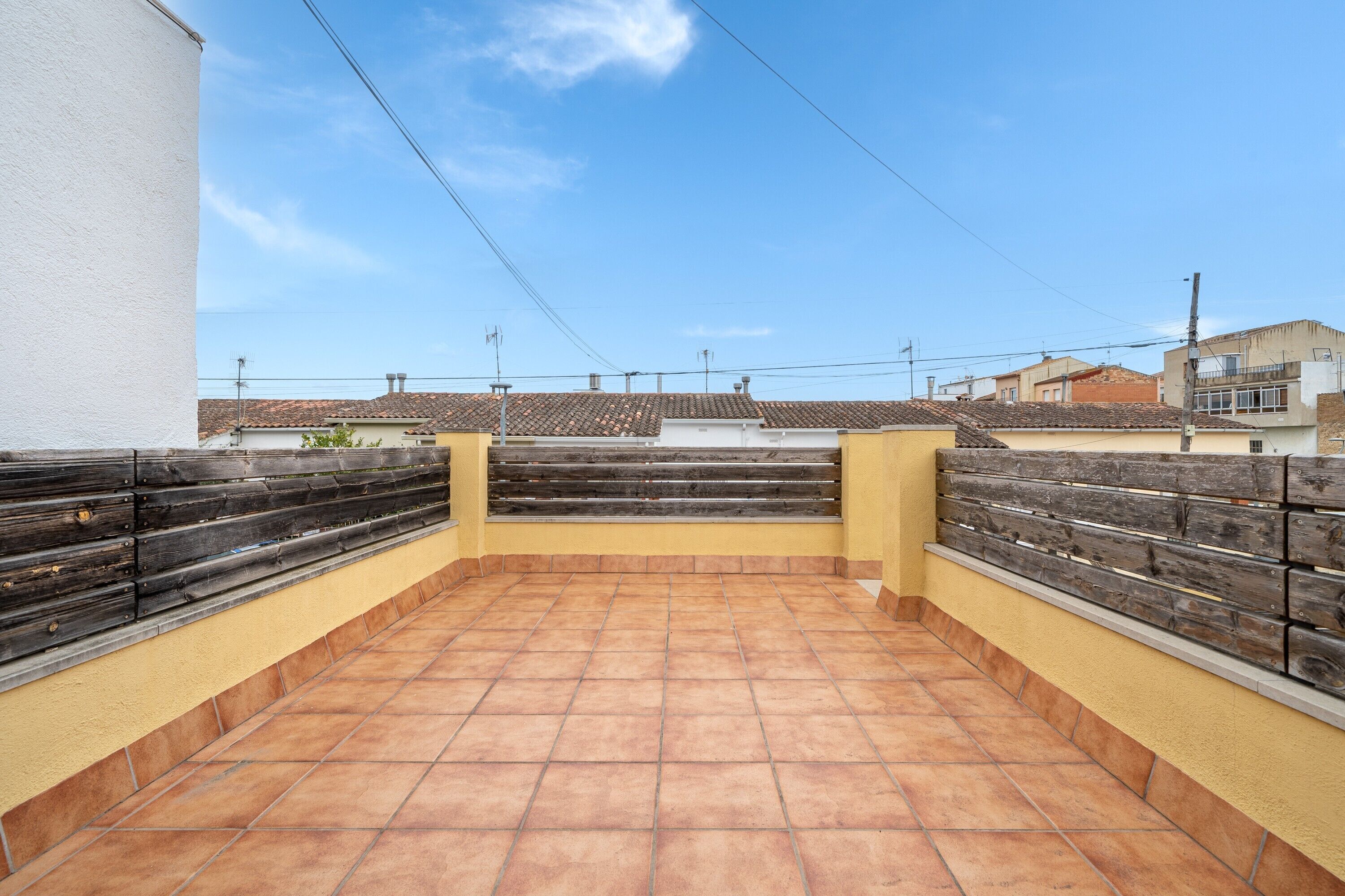 A rooftop terrace with tiled flooring, wooden railings, and a clear sky.
