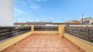 A rooftop terrace with tiled flooring, wooden railings, and a clear sky.