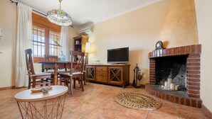 Una sala de estar con chimenea, televisor y comedor con sillas y mesa.