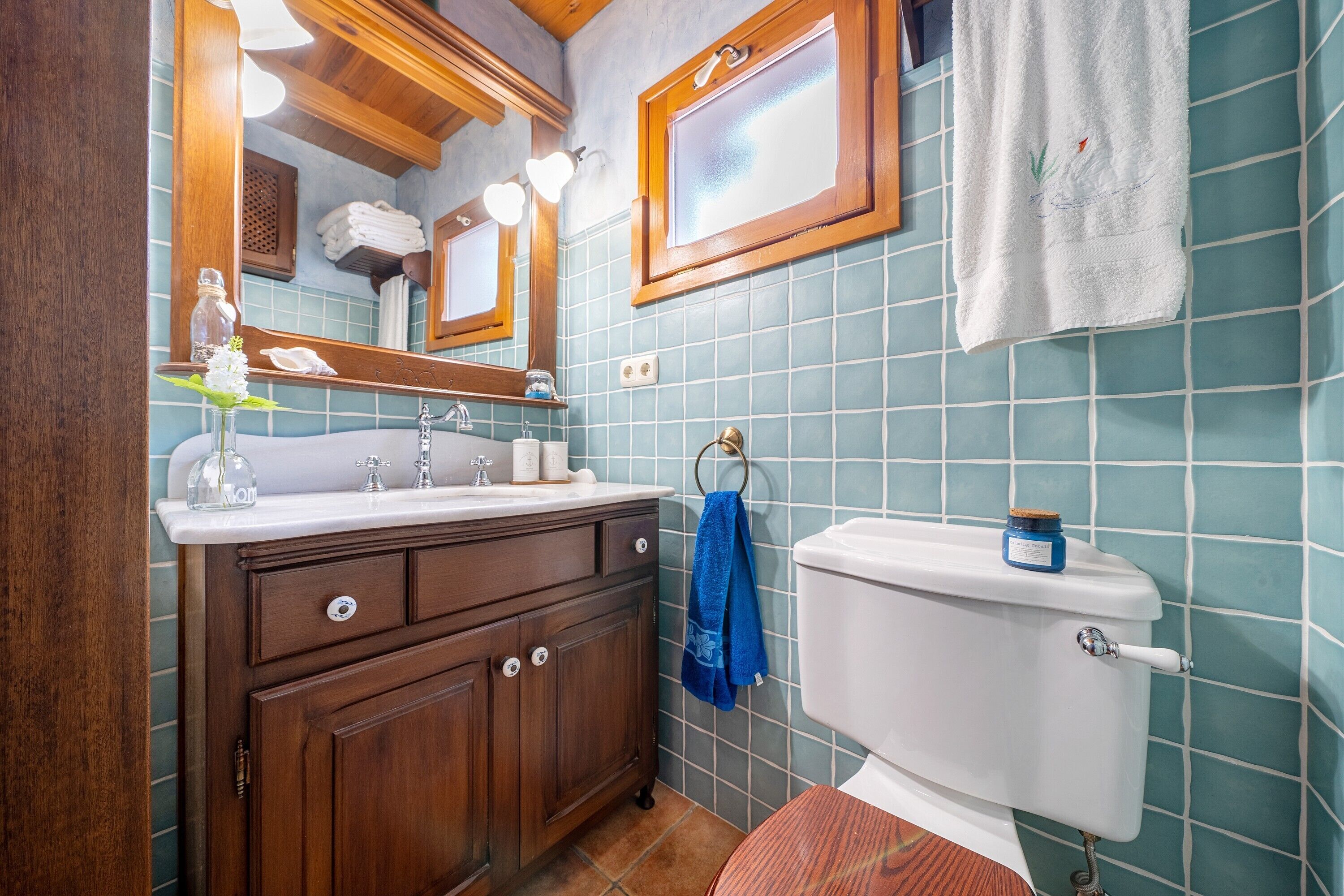 Een badkamer met een houten wastafelmeubel, een wit toilet en een blauwe betegelde muur.