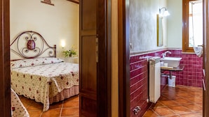 Une chambre à coucher comprenant un lit, une table de chevet, une fenêtre et une salle de bain avec un lavabo et un miroir.