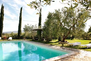 Una piscina con lettini, una pergola e alberi alti sullo sfondo.