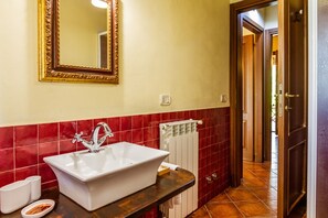 Un bagno con un lavandino bianco, uno specchio con cornice dorata, piastrelle rosse e una porta che dà su un'altra stanza.