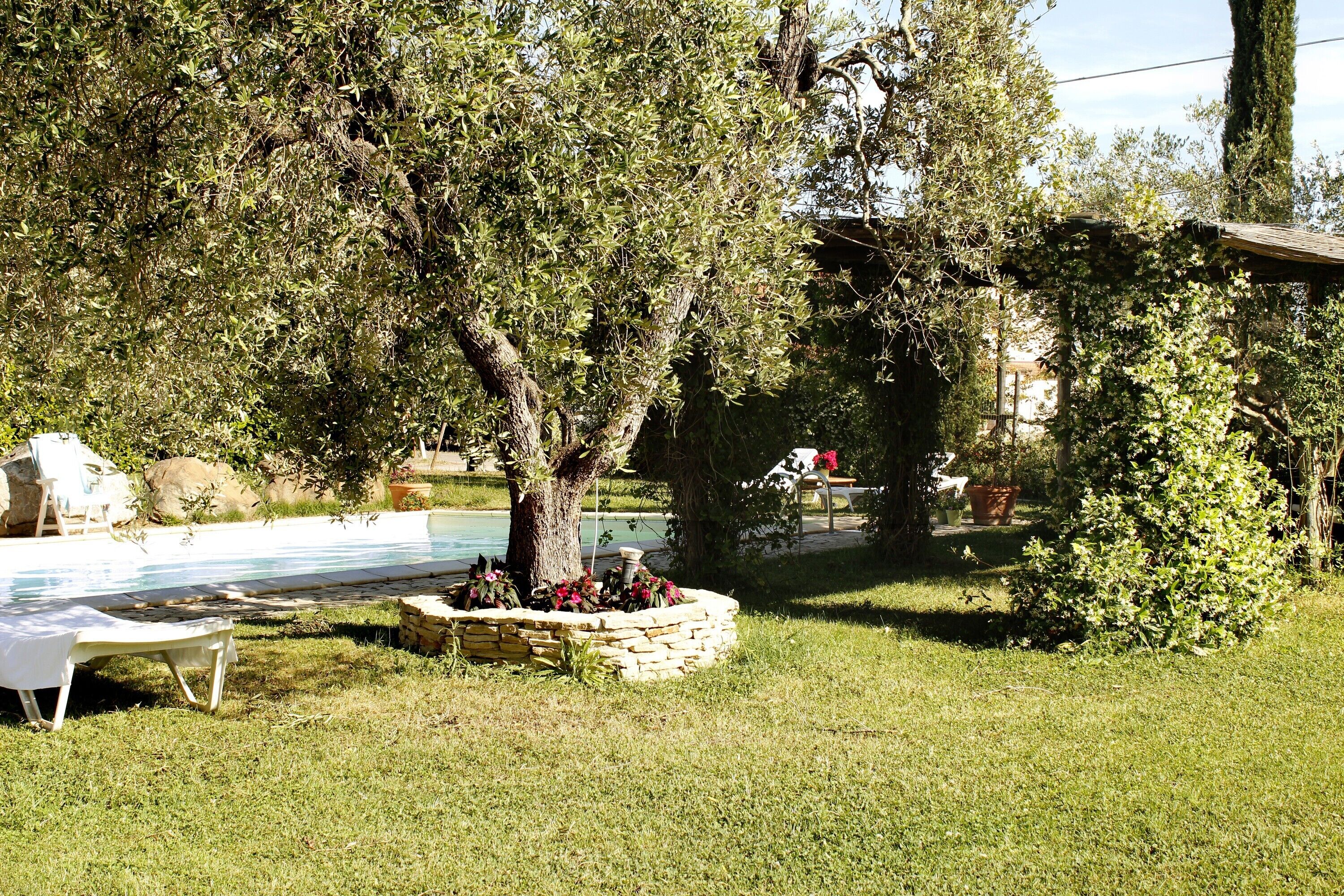 Un área de piscina con una jardinera de piedra, una silla blanca y un árbol.