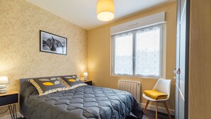 A bedroom with a large bed, a window with blinds, a chair, and a picture on the wall.