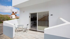Un edificio moderno con un molino de viento al fondo, una entrada con puerta de cristal y una pequeña zona de estar exterior.