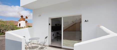 A modern building with a windmill in the background, a glass door entrance, and a small outdoor seating area.