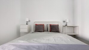Un lit bien fait, avec une tête de lit blanche, deux tables de chevet avec des lampes et un mur sobre.