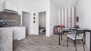 Une cuisine compacte équipée d’un lave-vaisselle, un coin repas avec une table et des chaises, et un espace de vie avec un canapé et un mur à rayures.