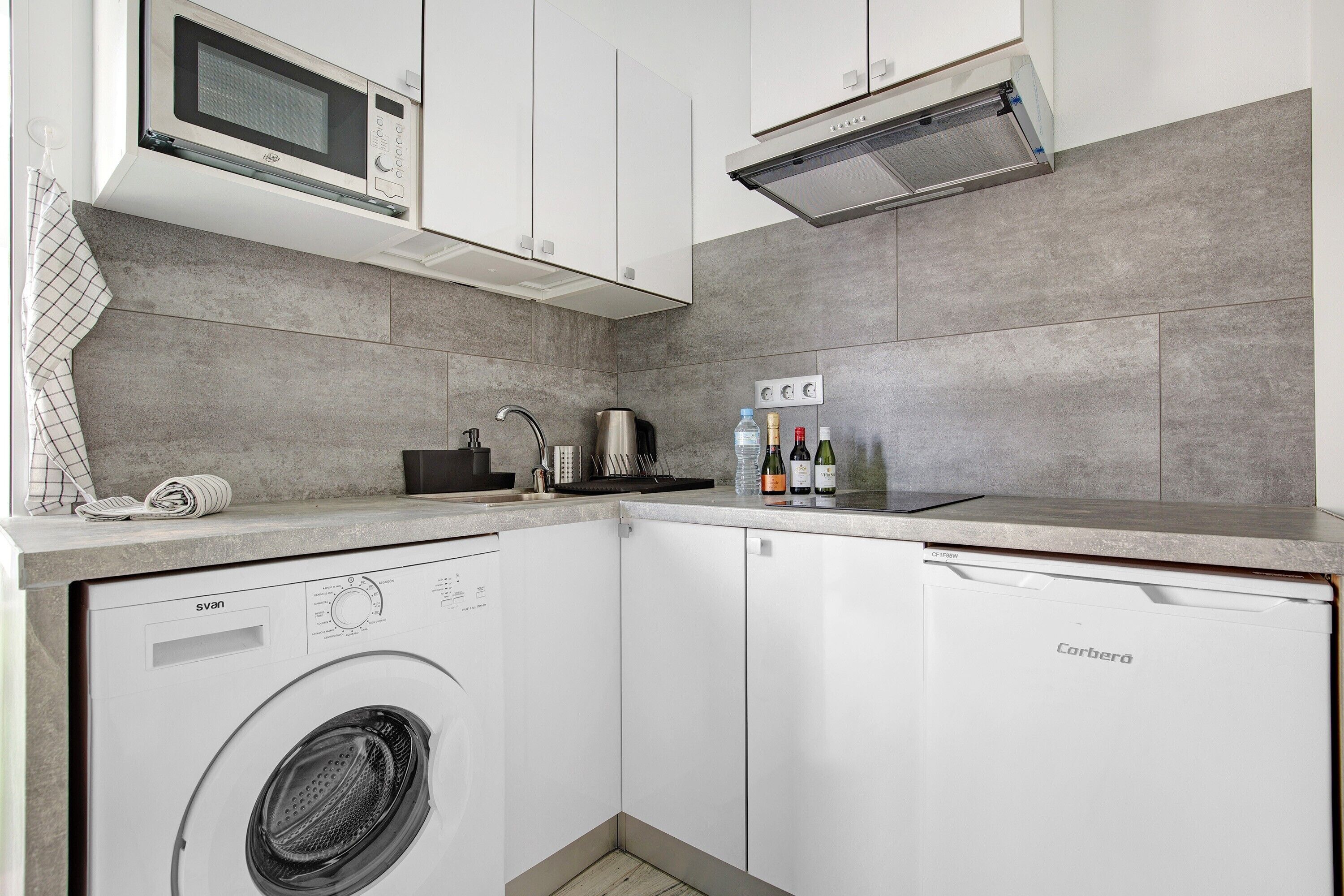 A compact kitchen with a washing machine, microwave, and a coffee maker.