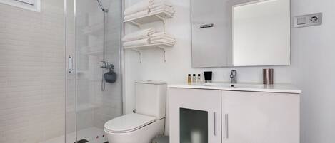 A modern bathroom with a glass shower enclosure, white toilet, and a cabinet with a mirror above it.