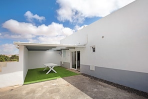 Une terrasse extérieure moderne, avec une table, un petit espace gazonné et un bâtiment à la façade blanche.