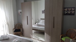 Een slaapkamer met een bed, een spiegel, een kledingkast en twee rieten stoelen.