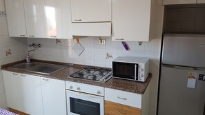 Eine Küche mit weißen Schränken, einem Gasherd, einer Mikrowelle und einem Kühlschrank.
