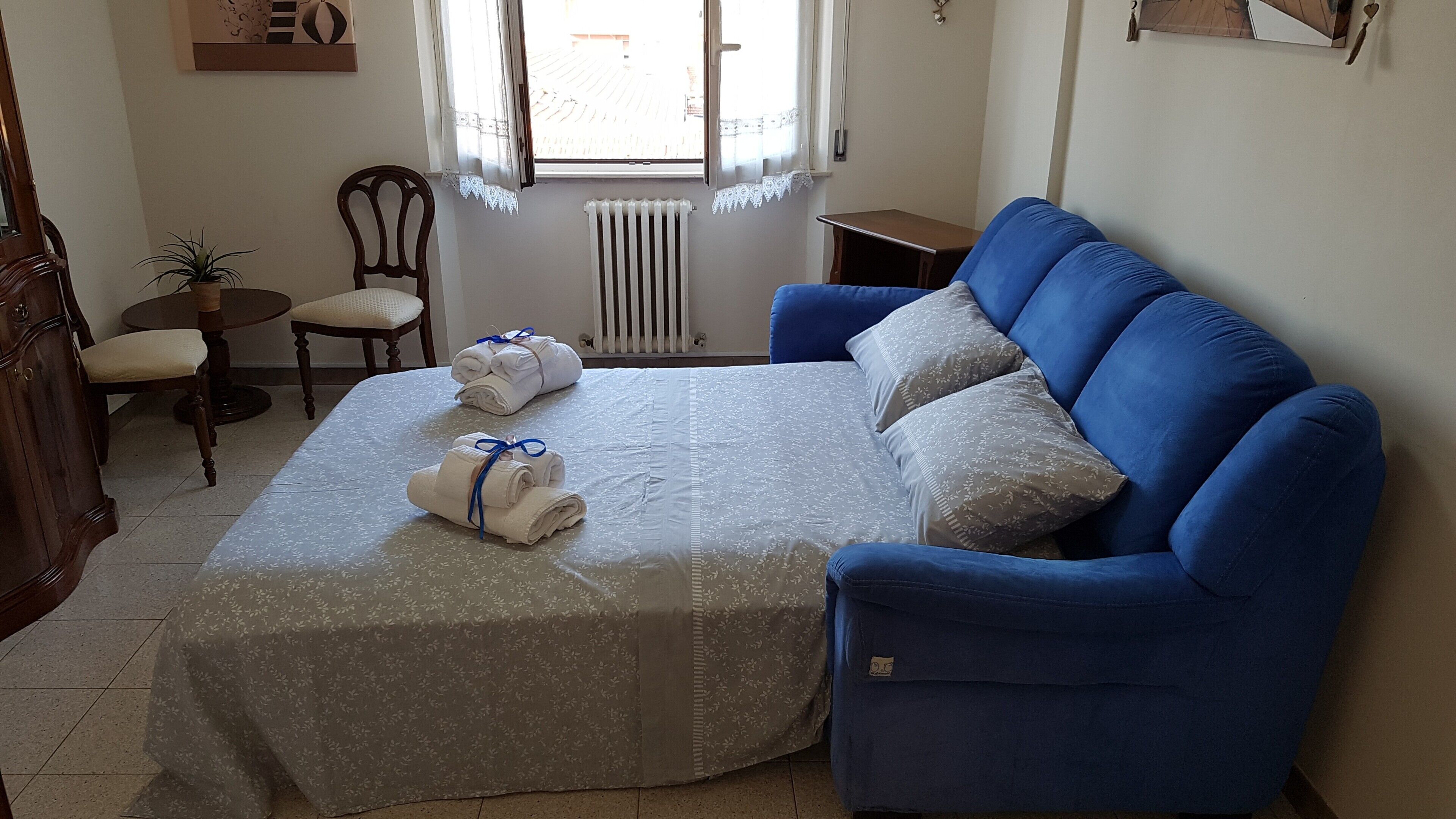 A bedroom with a bed, a blue armchair, a small table, a chair, and a potted plant.