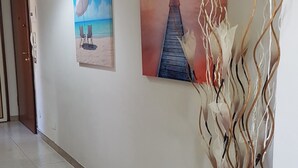Een gang met twee schilderijen aan de muur, een houten deur en een decoratieve plant.