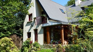 Een huis met een schuin dak, een balkon met planten en een tuin vol bloemen en struiken.