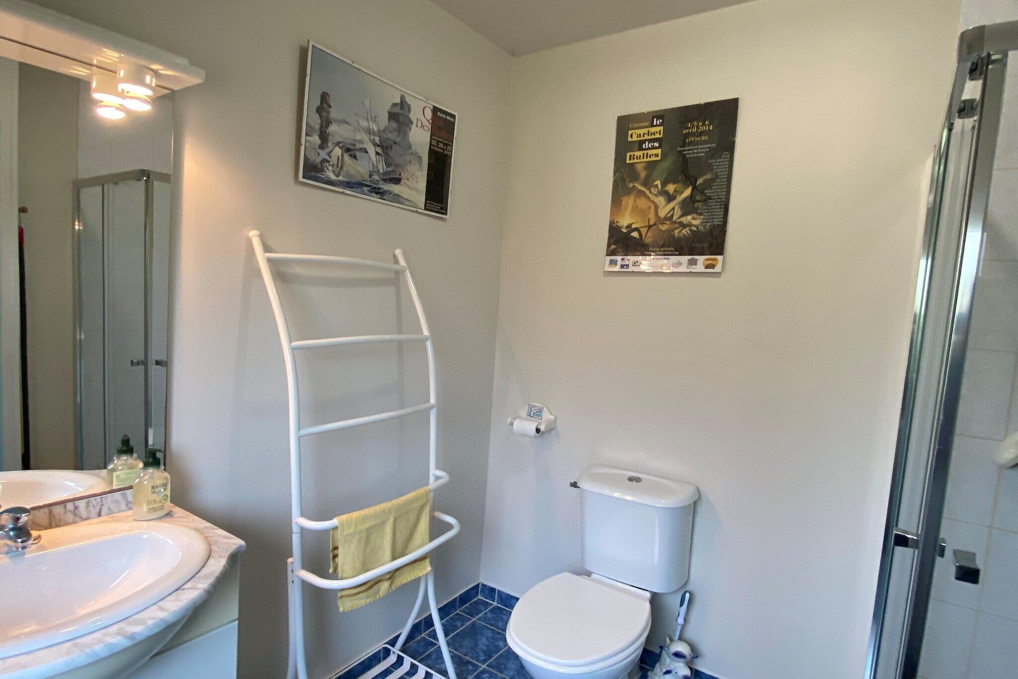 Un baño con lavamanos blanco, inodoro y cabina de ducha con mampara de vidrio.
