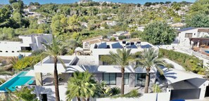 A modern villa with a swimming pool, solar panels, and a view of a hillside community. - Graham Holiday Rentals - Horizon (Moraira)